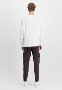 Weißes Langarmshirt mit rundem Ausschnitt, kombiniert mit dunkelvioletten Cargo-Hosen mit Seitentaschen und elastischen Bündchen, getragen mit weißen Sneakers.
