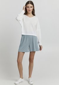 Vit, löst sittande stickad tröja med V-ringning. Matchad med ljusblå shorts med elastisk midja. Avslutad med vita sneakers.