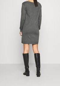 Abito sweater grigio con maniche lunghe, polsini a coste e vestibilità dritta, abbinato a stivali alti fino al ginocchio in pelle nera e uno sfondo semplice.