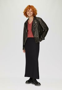 Schwarz, gerippt, knöchellange Rock, kombiniert mit einem roten Strickpullover und einer schwarzen Leder-Bikerjacke. Verfügt über silberne Beschläge und einen seitlichen Schlitz.