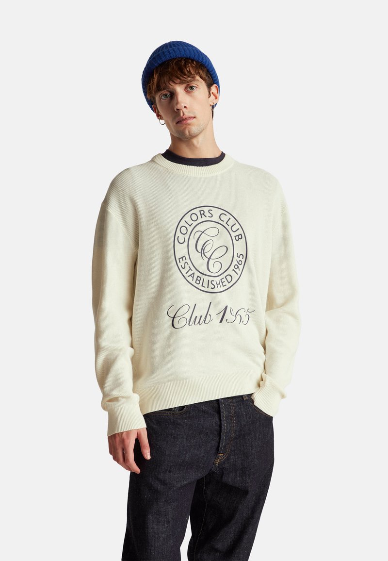 Crèmekleurige gebreide trui met geribbelde mouwen, voorzien van een cirkelvormig "Colors Club" logo en "Club 1955" tekst in donkerblauw.
