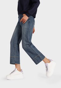 Culotte in denim con taglio cropped, colore blu, sneakers platform bianche con dettagli in lavanda e laccio, vista laterale.
