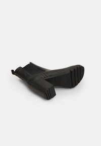 Botine negre cu superior sintetic neted, dotate cu toc bloc și talpă texturată, concepute pentru a fi purtate ușor cu ajutorul unei bucle.