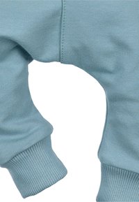 Jasnoniebieskie bawełniane dresy z żeberkowymi mankietami, o gładkiej fakturze i wycięciem na kostce. Szczegółowe przeszycia wzdłuż szwów.