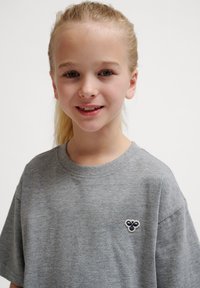 Graues kurzärmliges T-Shirt mit Rundhalsausschnitt und kleinem gesticktem Logo auf der Brust. Weicher, leichter Stoff mit glatter Textur.