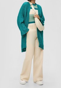 Türkisfarbener Strick-Cardigan über einem gestreiften Grün- und Cremetop, kombiniert mit beigen weiten Hosen und weißen Sneakers. Verstellbare cremefarbene Umhängetasche.