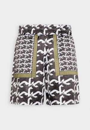 Pantaloni corti a pois bianchi e neri con vita elasticizzata e decorazioni verdi e dorate, caratterizzati da forme geometriche throughout il design.