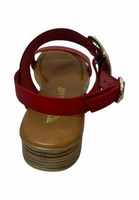 Sandalia roja con tacón plano, que cuenta con una suela marrón gruesa de textura estratificada, correa ajustable y herrajes decorativos dorados.