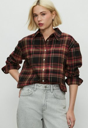 Red and black plaid shirt with a button-down collar, long sleeves rolled at the cuffs, and a relaxed fit. Worn with light gray high-waisted jeans.