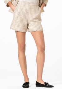 Beiga tweed-shorts med ett texturerat mönster, fransad fåll och sidofickor, i kombination med svarta ballerina-skor med en rosett-detalj.