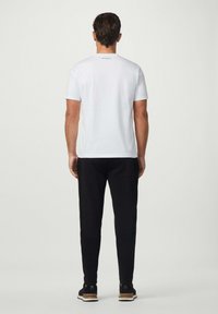 Bílá krátká tričko s kulatým výstřihem, spárované s černými zúženými kalhotami se bočními pruhy a sportovními teniskami s texturovanou podrážkou.