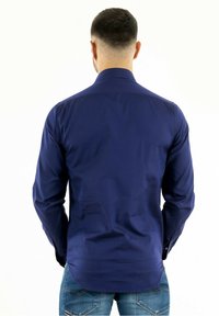 Mörkblå långärmad skjorta i slät tyg, med krage och knäppta manschetter. Baksidan är enkel med en böjd nederkant.