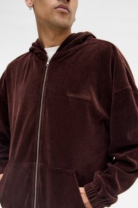 Hnědá kordurová zipová mikina s ribbovanou texturou, obsahující přední kapsu, elastické manžety a decentní logo na hrudi.