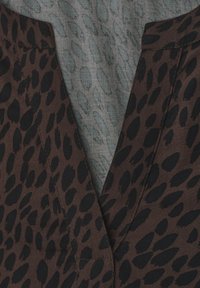 Tissu marron avec des taches noires irrégulières ressemblant à un imprimé animal, plié pour montrer un décolleté en V avec des coutures visibles.