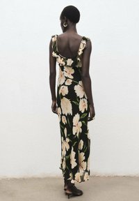 Zwarte maxi-jurk met grote beige bloemen, ruches aan de mouwen en een lage rug. Gladde stof met een vloeiende silhouet.