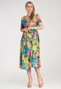 Blumenkleid in Midi-Länge mit kurzen Ärmeln in lebhaften Farben, das große Blüten auf einem beigen Hintergrund zeigt, aus leichtem Stoff gefertigt.