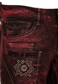 Rode denim jeans met een versleten textuur, voorzien van gele stiksels, een logo op de achterzak en een klein voorvak.