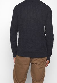 Gebreide marineblauwe trui met een textuurpatroon, geribde manchetten en zoom, ronde halslijn, gecombineerd met tan kleurige broek.