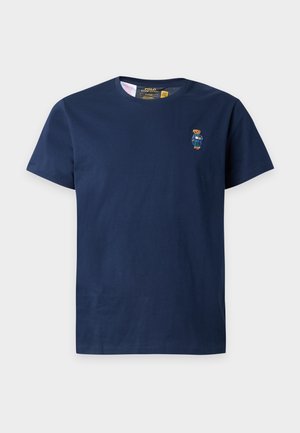 Marineblaues T-Shirt mit kurzen Ärmeln und Rundhalsausschnitt sowie einem kleinen bestickten Bären in blauer Kleidung auf der linken Brust.