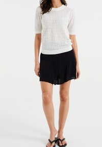 Haut tricoté blanc à manches courtes avec un motif texturé, associé à une jupe noire fluide. Les chaussures sont des tongs noires.