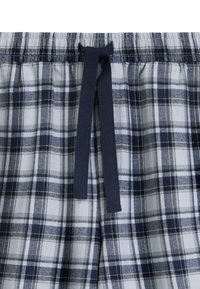 Elastyczny pas z granatowym sznurkiem na białych spodniach lub szortach w kratę w granatowo-białym kolorze.