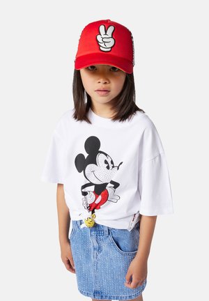 Witte T-shirt met een zwart en rood Mickey Mouse-print, gecombineerd met een lichtblauwe denimrok. Rode pet met een witte vredestekenafbeelding.