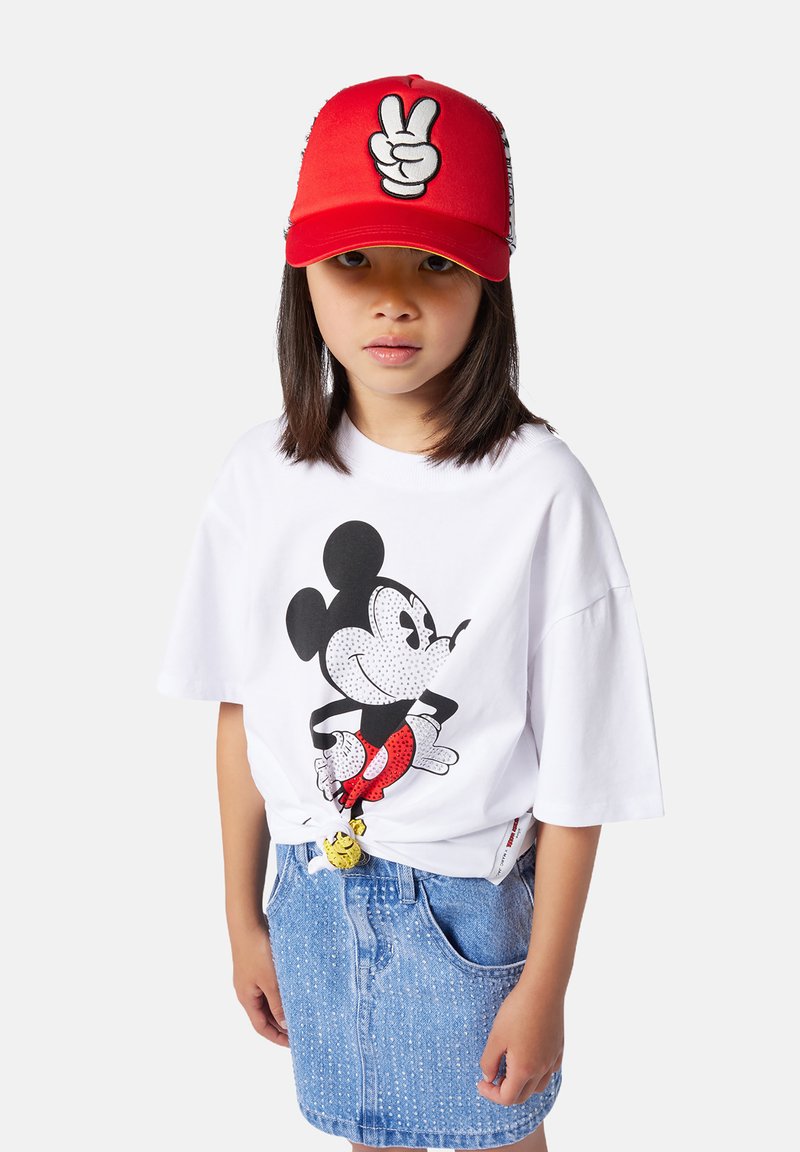 T-shirt bianco con stampa di Topolino nera e rossa, abbinato a una gonna di jeans azzurro chiaro. Cappellino rosso con grafica di un simbolo di pace bianco.