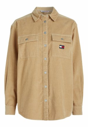 Camisa de pana en tono marrón claro con cierre de botones en la parte frontal, dos bolsillos en el pecho, botones plateados y un pequeño logo bordado en el bolsillo izquierdo.