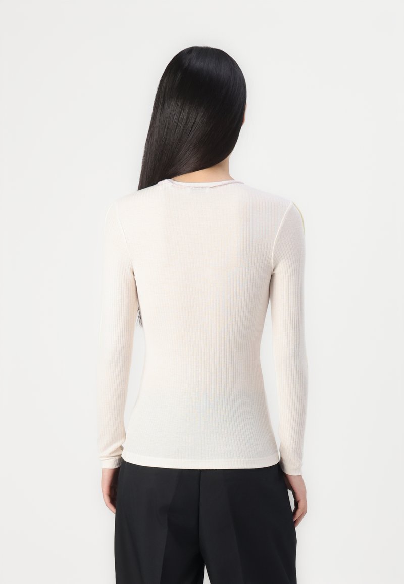 Langärmliges, geripptes Shirt in hellem Beige, aus elastischem Stoff gefertigt. Enganliegende Silhouette mit Rundhalsauschnitt und minimalistischen Nähten am Rücken.