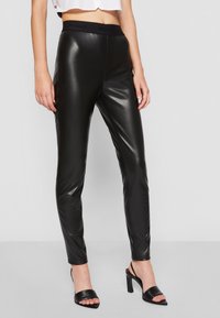 Leggings en faux cuir noir avec une large ceinture élastique mettant en avant le nom de la marque "HUGO". Texture lisse et coupe ajustée.