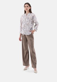 Lightweight, floral-patterned blouse with button placket and pleats. Paired with loose, neutral-colored trousers and heels.