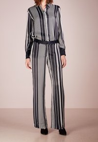 Black and white striped silk shirt and wide-leg pants set, featuring a collar, long sleeves, and a belted waist. Smooth texture, tailored fit.