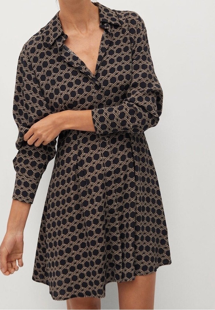 Femme portant une robe noire à manches longues avec un motif hexagonal géométrique beige, col et taille ajustée.