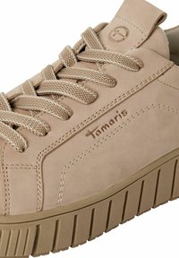 Beige suède sneaker met geweven veters, een gevoerde kraag en een dikke, geribbelde zool. Heeft een reliëflogo en contrasterende stiksels.