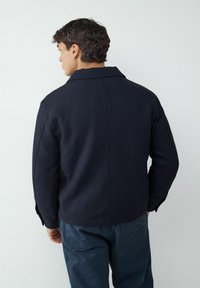 Granatowa, wełniana marynarka z mieszanką materiałów, z sztywnym kołnierzem i zapinanymi mankietami; charakteryzuje się czystym szwem z tyłu oraz teksturowanym materiałem.