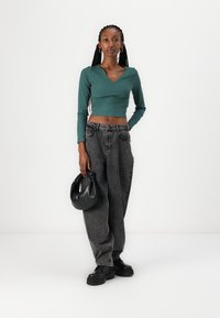 Grønn langermet crop topp, høy midje, løse grå jeans, kraftige sorte plattform sko, og en svart rund håndveske.