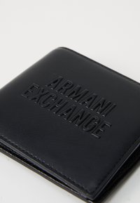 Portafoglio in pelle nera con logo "ARMANI EXCHANGE" in rilievo sulla parte anteriore, che mostra una superficie liscia e bordi cuciti.