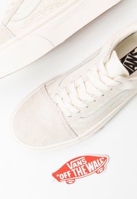 Baskets Vans blanches en suède et toile, avec un bout lisse et des lacets plats. Comprend un autocollant du logo Vans rouge en dessous.