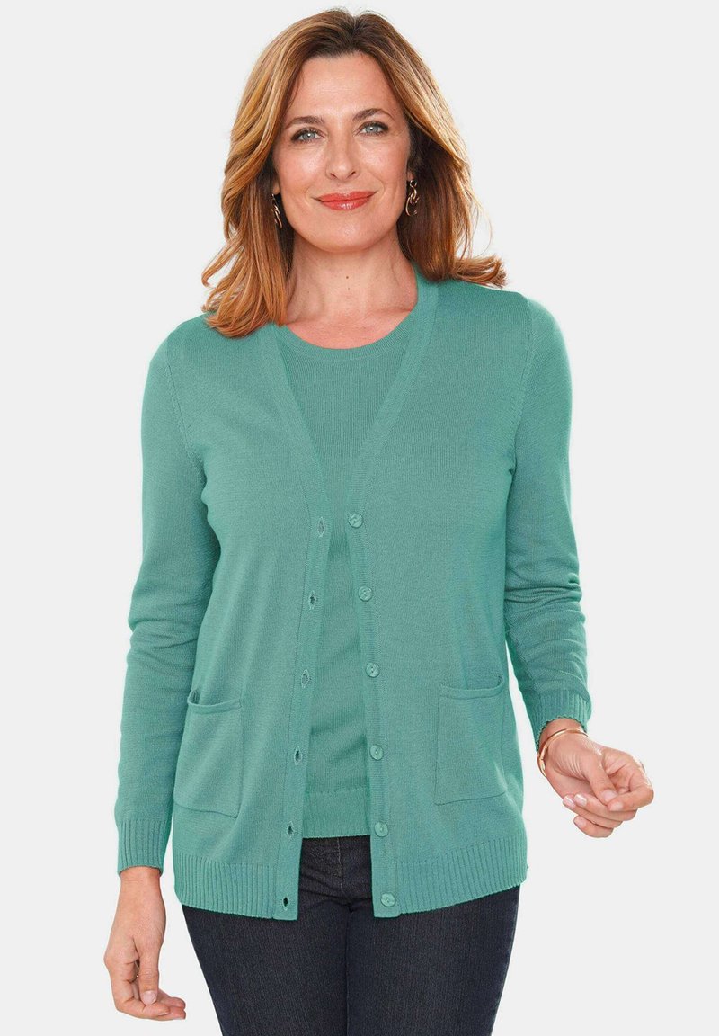 Strickjacke in Türkis mit V-Ausschnitt, Knopfverschluss und zwei vorderen Taschen. Lange Ärmel mit gerippten Bündchen und Saum. Kombiniert mit einem passenden Oberteil.