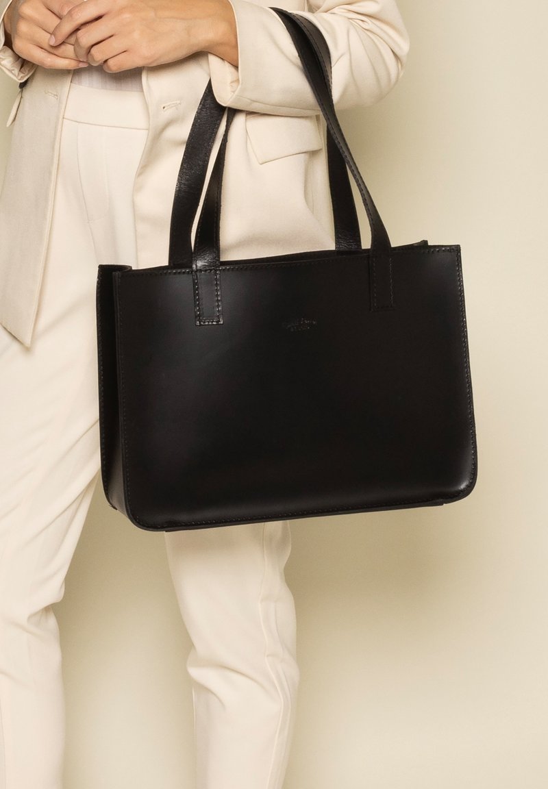 Sac fourre-tout en cuir noir avec deux poignées robustes, forme rectangulaire, texture lisse et détail de logo discret à l'avant.