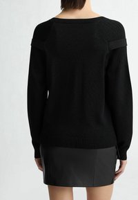 Pull en maille noire avec accents côtelés, large encolure et épaules tombantes, associé à une minijupe en cuir noir. Texture lisse dans l'ensemble.
