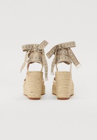 Béžové espadrilové sandály na platformě s tkanými juty a ozdobnými vzorovanými stužkami uvázanými kolem kotníku. Otevřená zadní část.