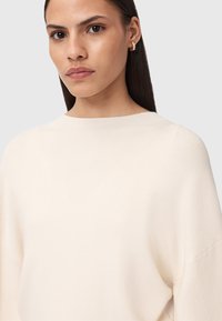 Maglione lavorato a maglia color crema con scollatura a barca, texture a costine e maniche ampie. Design semplice senza motivi o elementi hardware visibili.