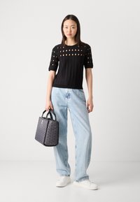 Black knit top with textured panels and cutouts, paired with light blue high-waisted jeans and a patterned dark bag. White sneakers included.