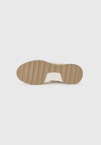Suola di sneaker in gomma beige con scanalature e creste pronunciate, con un accento bianco sul tallone. Texture liscia con una forma arrotondata.