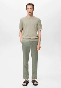 Tricou din bumbac verde deschis, cu mâneci scurte, asortat cu pantaloni verzi deschisi și sandale negre. Design simplu, ajustat.