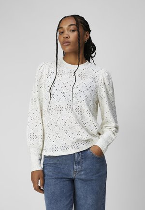 White, textured blouse with intricate eyelet pattern, round neck, and puff sleeves, paired with blue jeans.