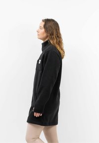 Zwarte fleece jack met hoge kraag, voorkantzak en lange mouwen. Gelaagd stof en een ontspannen pasvorm, tot halverwege de dij.