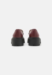 Bordeaux leren schoenen met een ronde neus en een zwarte stevige zool. Het ontwerp heeft minimale accenten en een gladde textuur.