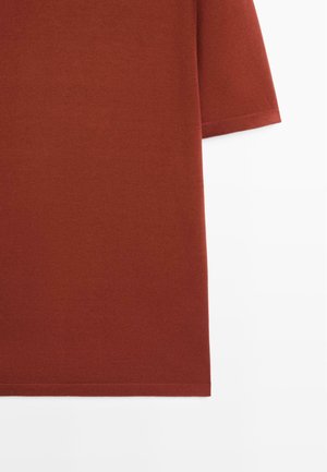 Robe en tissu de couleur rouille avec manches mi-longues et ourlet droit sur fond blanc.